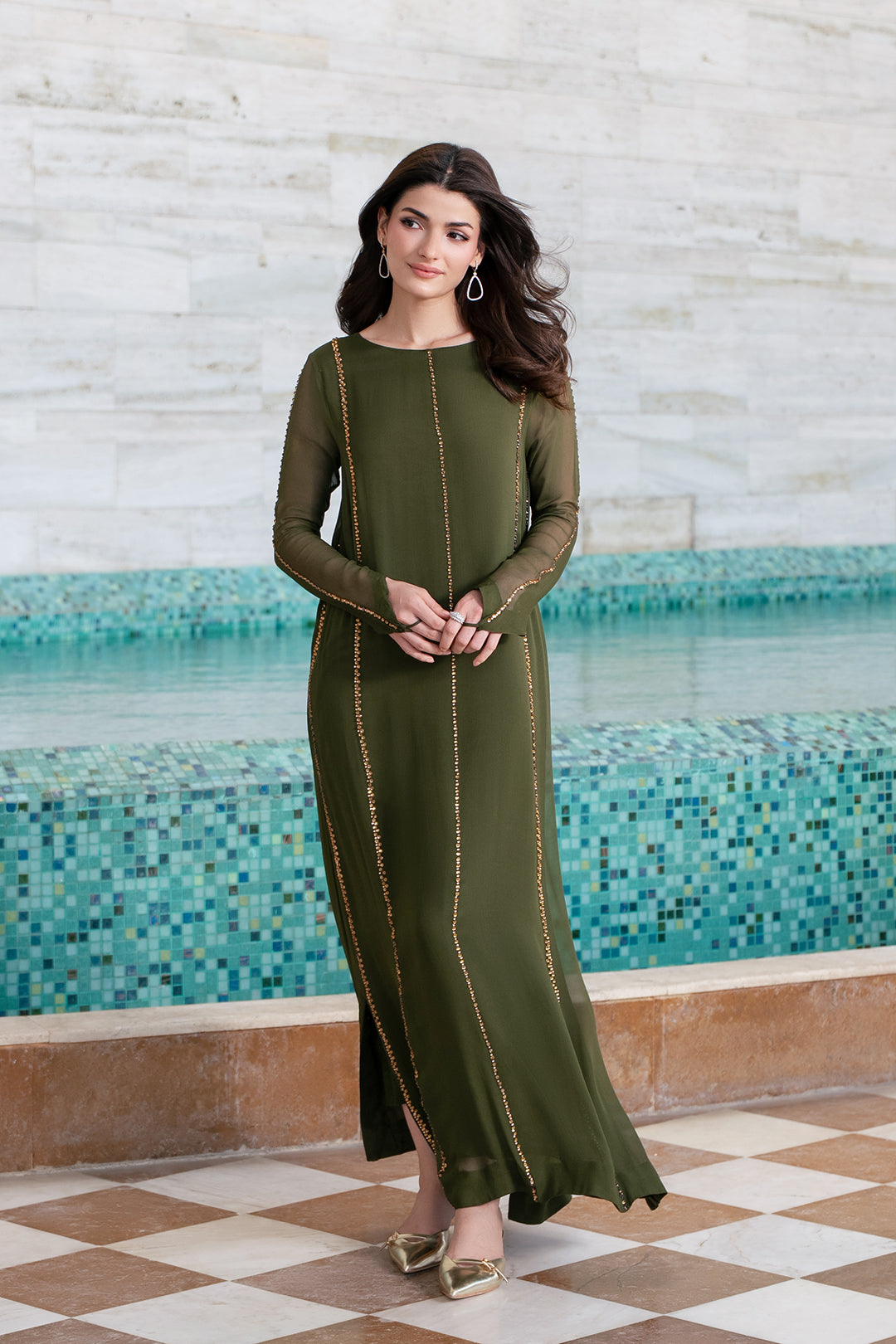 Woman in a green dress standing in front of a pool with mosaic tiles wearing a viral handmade dress.